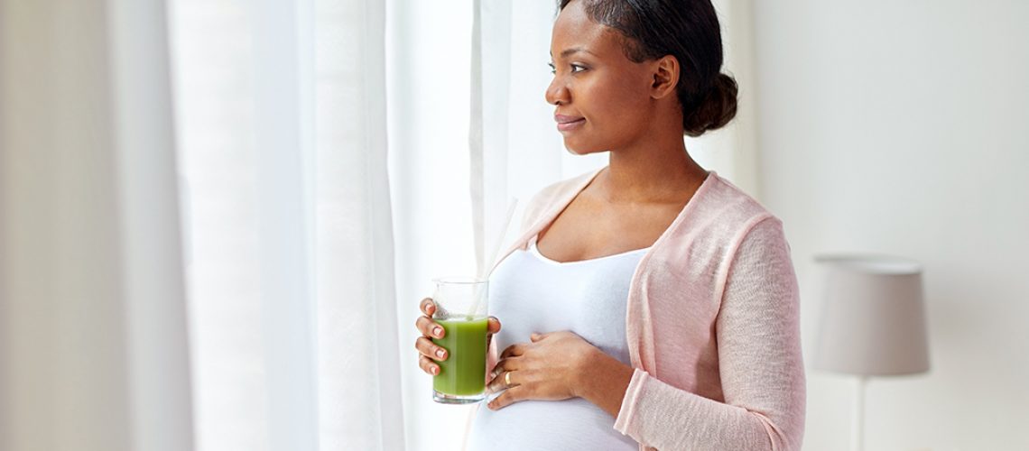 pregnancy, people and rest concept - happy pregnant african american woman drinking green vegetable juice or smoothie at home